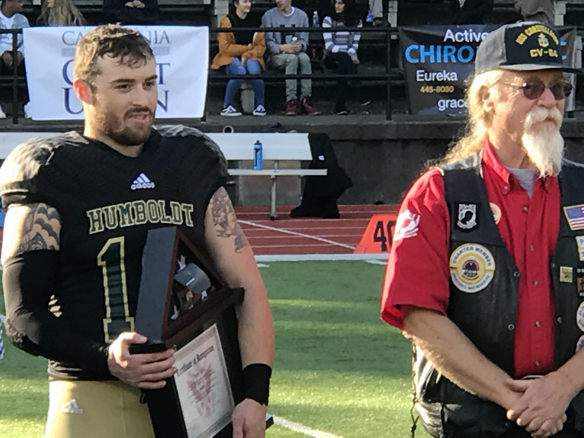 A Humboldt Heroes honoree holding a framed flag case during a field-side recognition